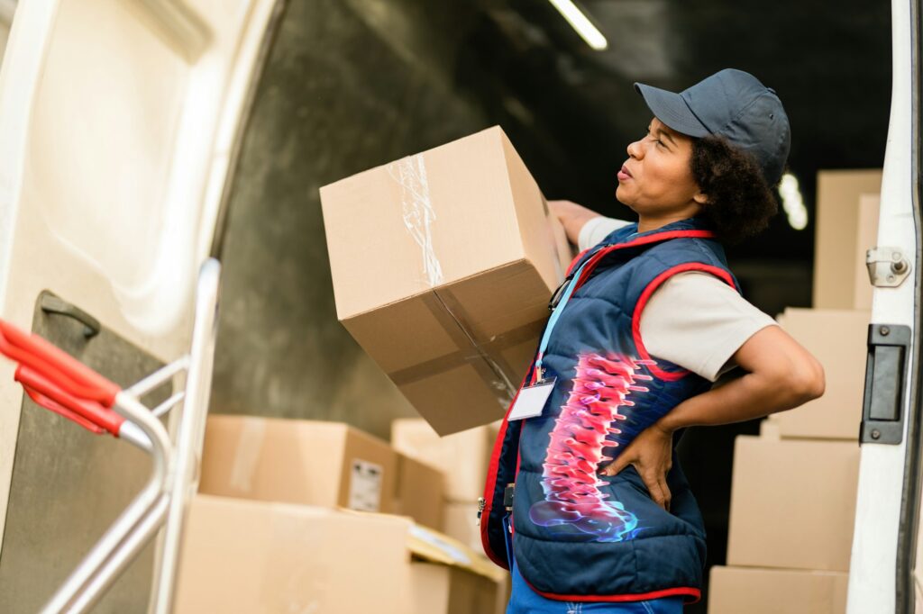 Female African American deliverer having lover back pain while loading packages in a van.