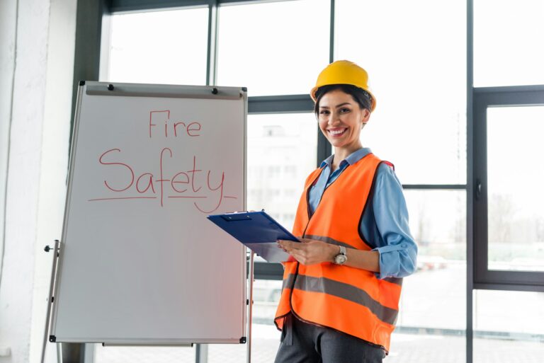 happy female firefighter in helmet holding clipboard and pen while standing near white board with