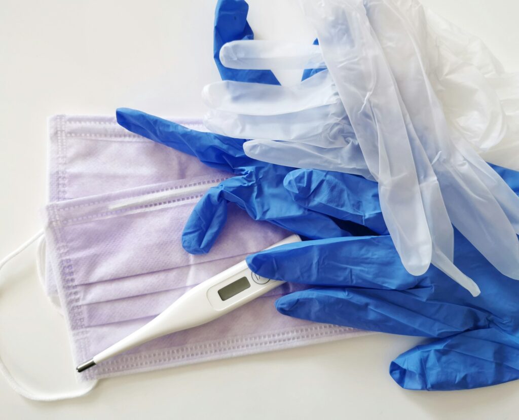 Overhead, top view of medical supplies. Face mask, gloves and thermometer on white background.