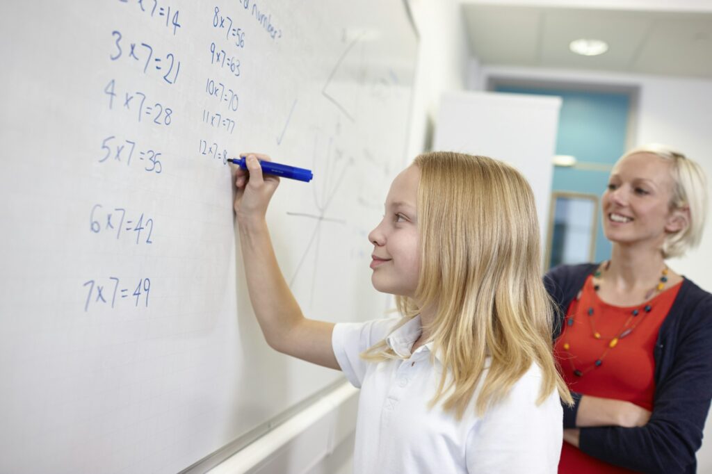 Schoolgirl doing multiplication on white board